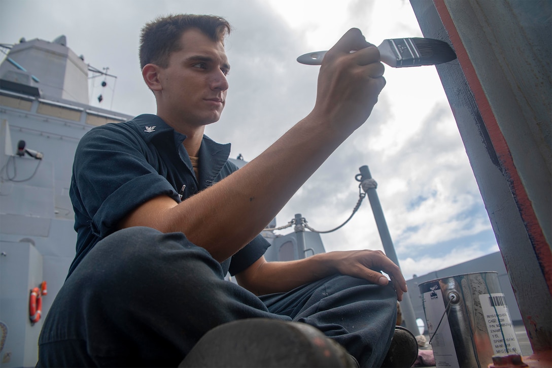 A sailor paints part of a ship.