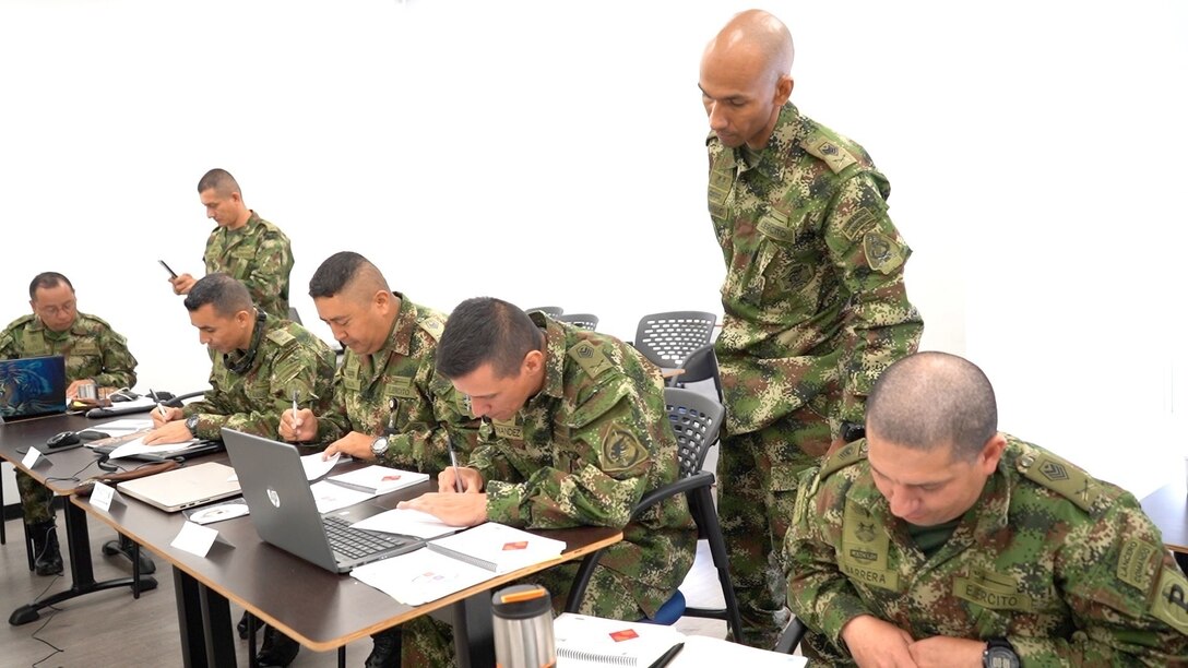 Military personnel sit at desks.