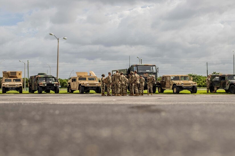 Soldiers stand in front of vehicles.