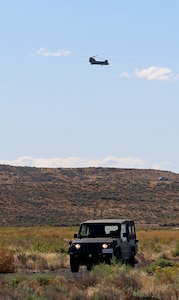 Soldiers of the Japan Ground Self-Defense Force participate in field training while a U.S. CH-47 Chinook passes behind during Rising Thunder, Sep. 1, at the Yakima Training Center in Yakima, Washington.