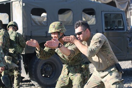 Pfc. Darian Matos  and a Japanese infantryman mimic a rifle stance with their hands, as soldiers watch, Sep. 2, while on Range 15 at Yakima Training Center, during exercise Rising Thunder 19.