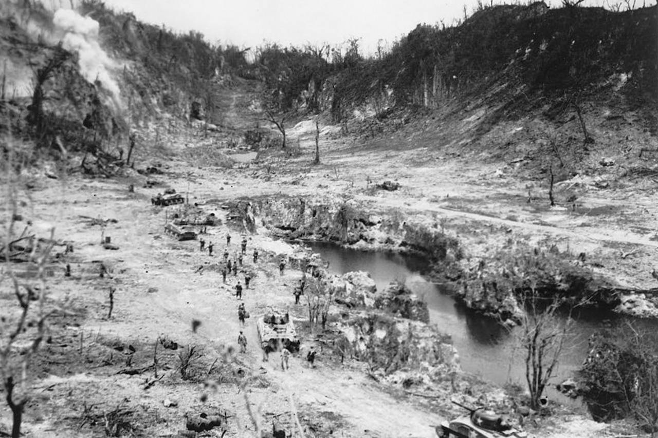 Men and tanks move toward a bombed-out ridge. A small lake is to their right.