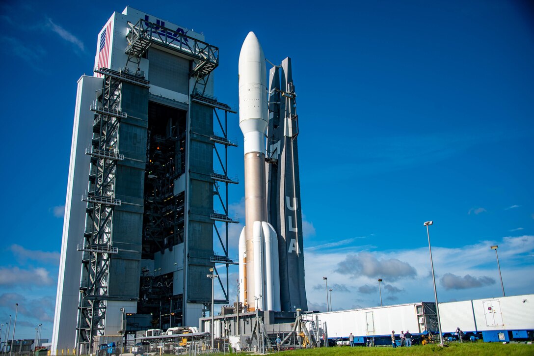 A large rocket stands next to a launch tower against a deep blue sky.