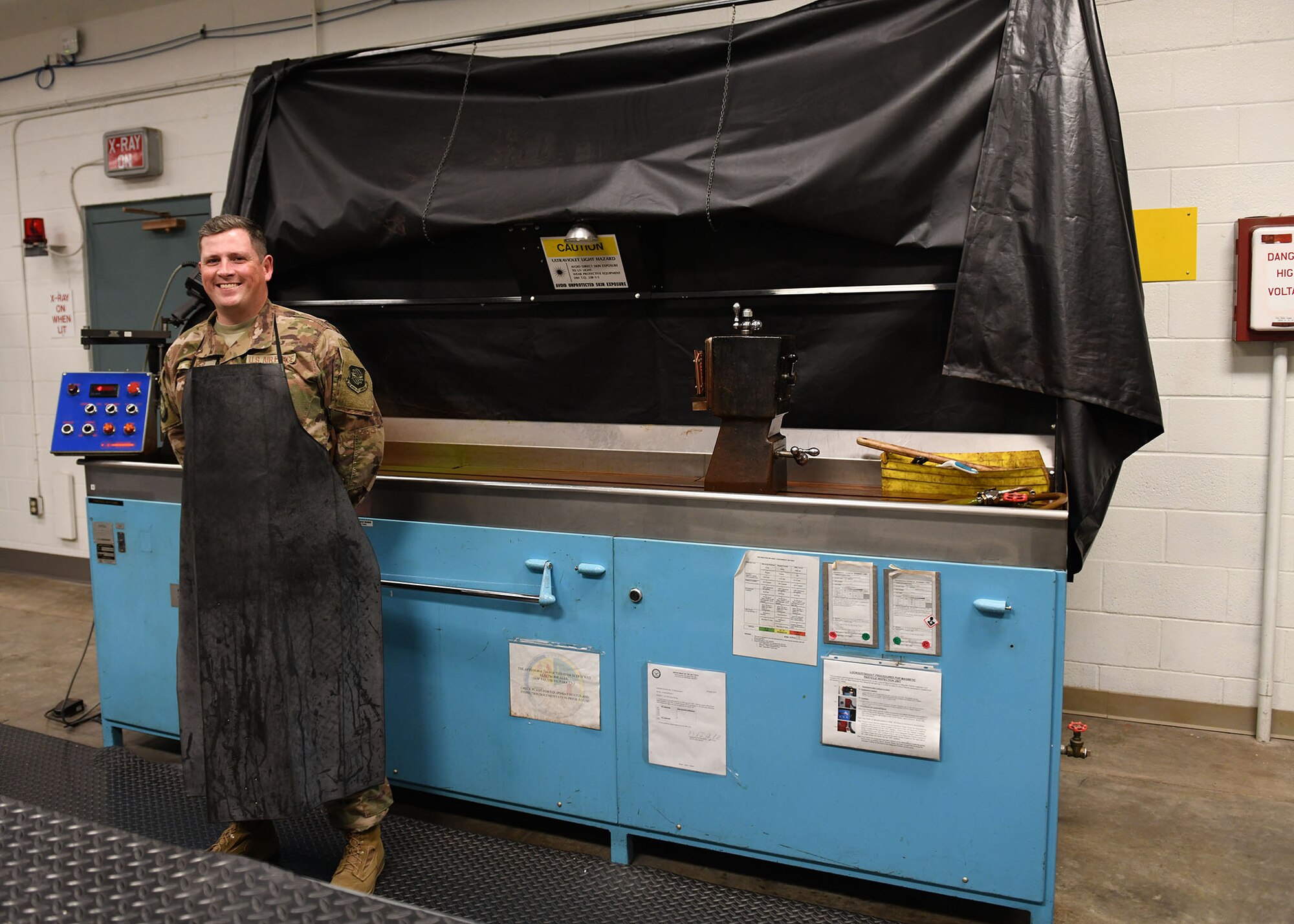 A man with a black protector stands in front of a blue machine.