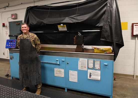 A man with a black protector stands in front of a blue machine.