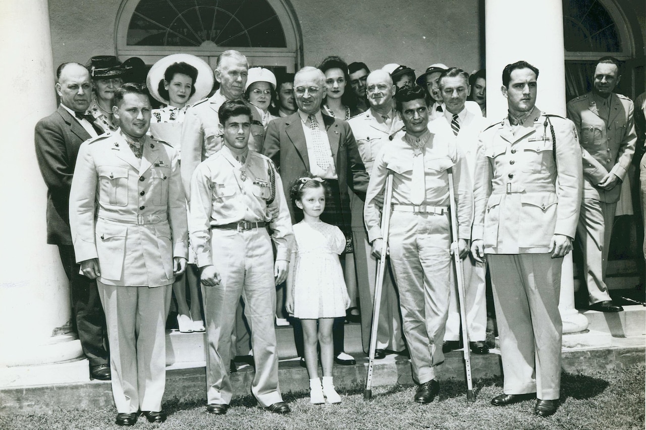 A group, including four service members wearing Medals of Honor, stands on a lawn with President Harry S. Truman and their families.