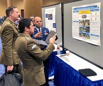Lt. Col. Luis Berrios, 433rd Aeromedical Staging Squadron chief nurse and 433rd Medical Group chief of education and training, speaks to an Australian Army major and captain, about his quality improvement project titled "Addressing Reserve Joint-Service Medical Training Gaps through Multi-Faceted Expeditionary Simulation" at the 2019 Military Health System Research Symposium, Aug. 20, 2019 in Kissimmee, Florida.