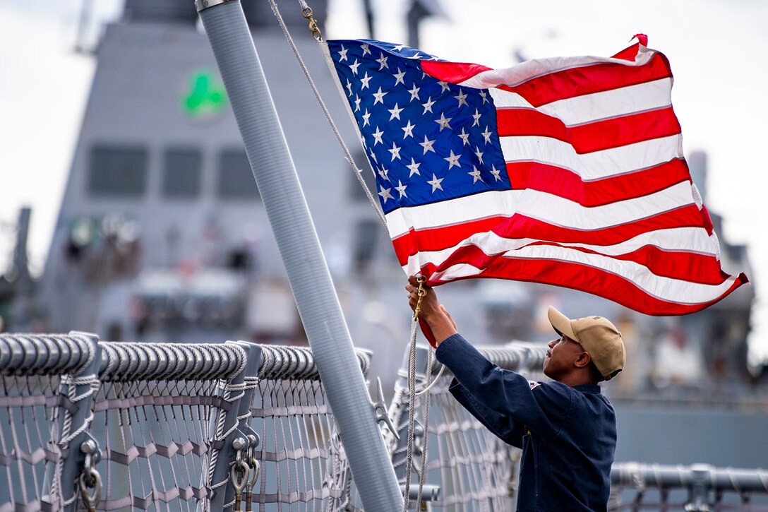 A sailor lowers a flag on a ship.