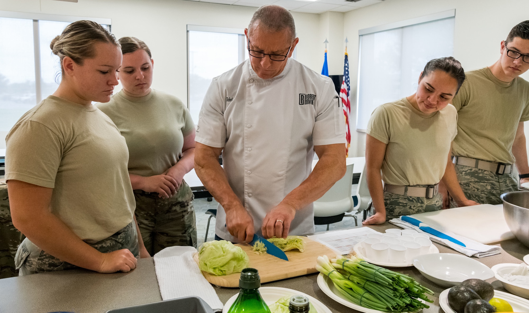 Robert Irvine demonstrates how to shred lettuce to Airmen