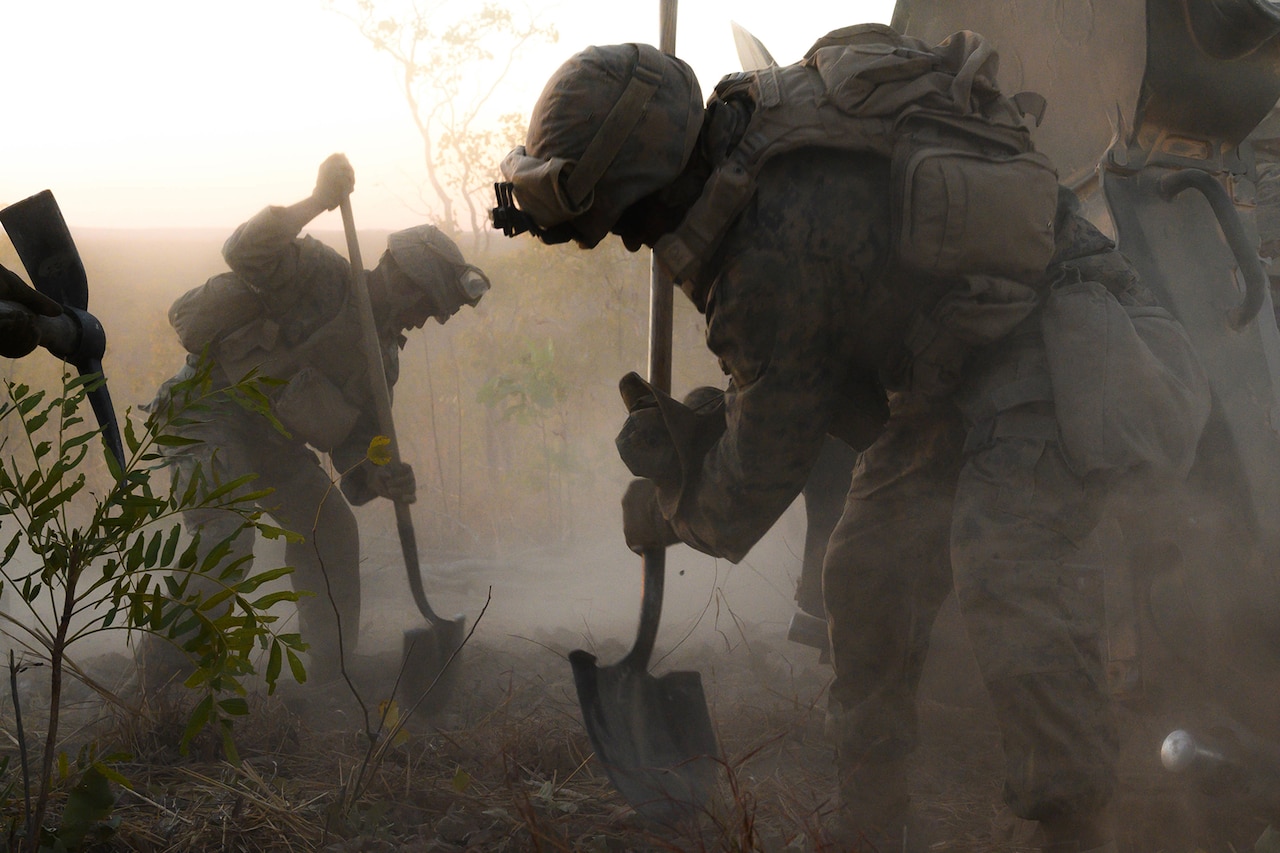 Marines shovel dirt to support a howitzer.