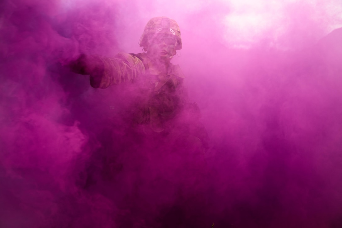 A soldier is seen through purple smoke.