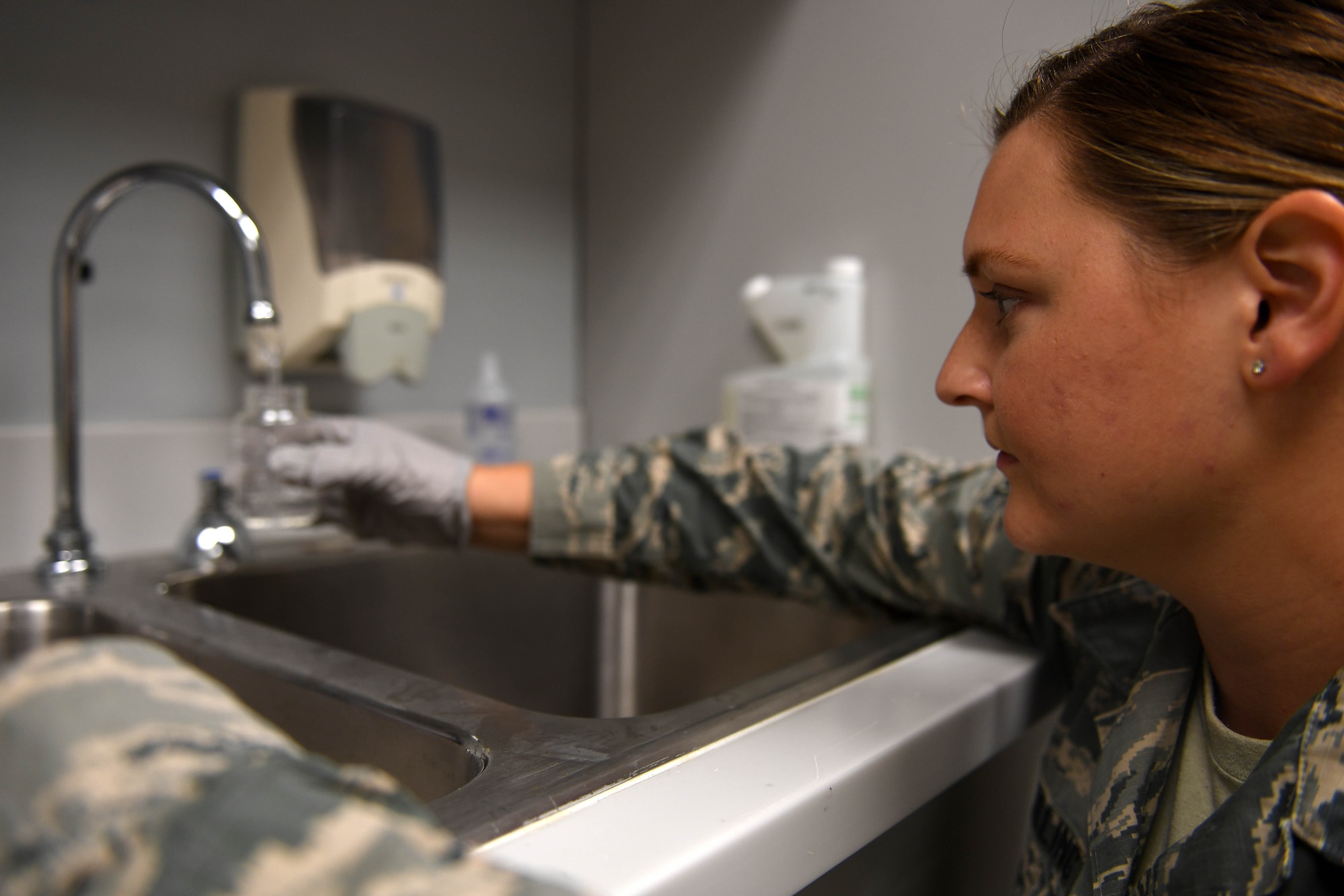A woman wearing ABUs gets water from a faucet.