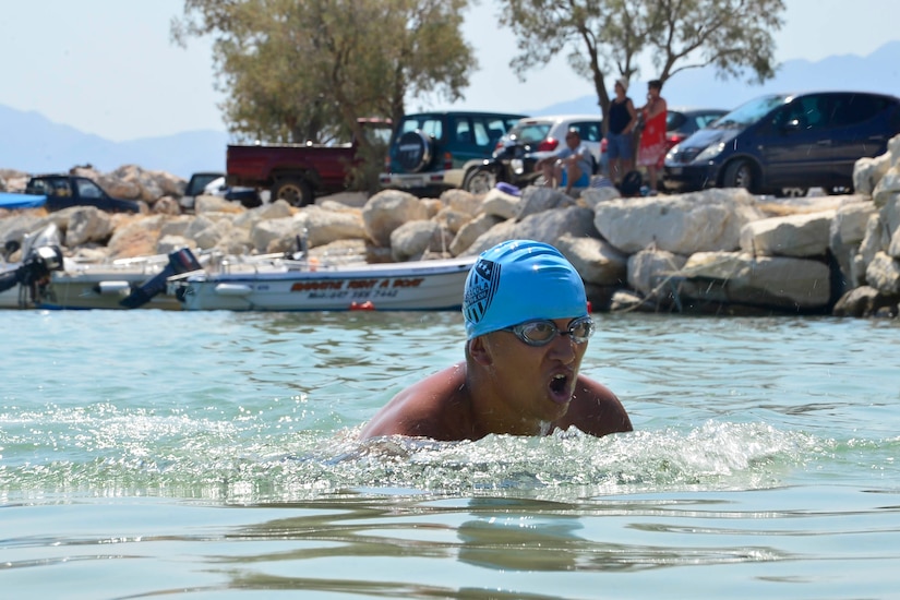 A man wearing goggles and a blue bathing cap swims.