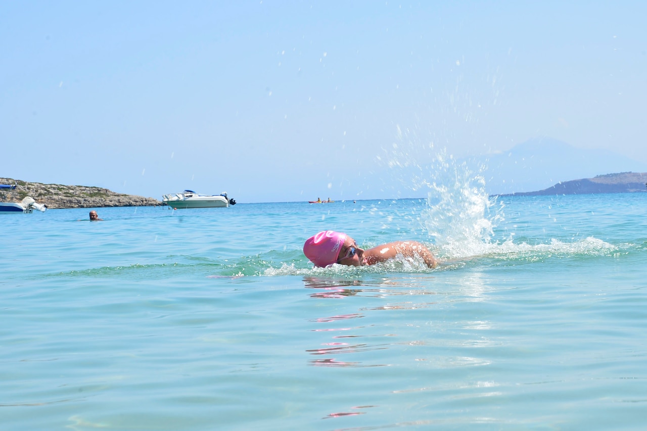A woman wearing goggles and a pink bathing cap swims.