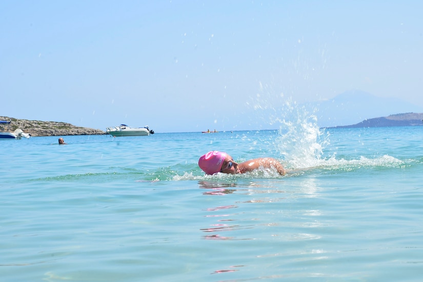 A woman wearing goggles and a pink bathing cap swims.