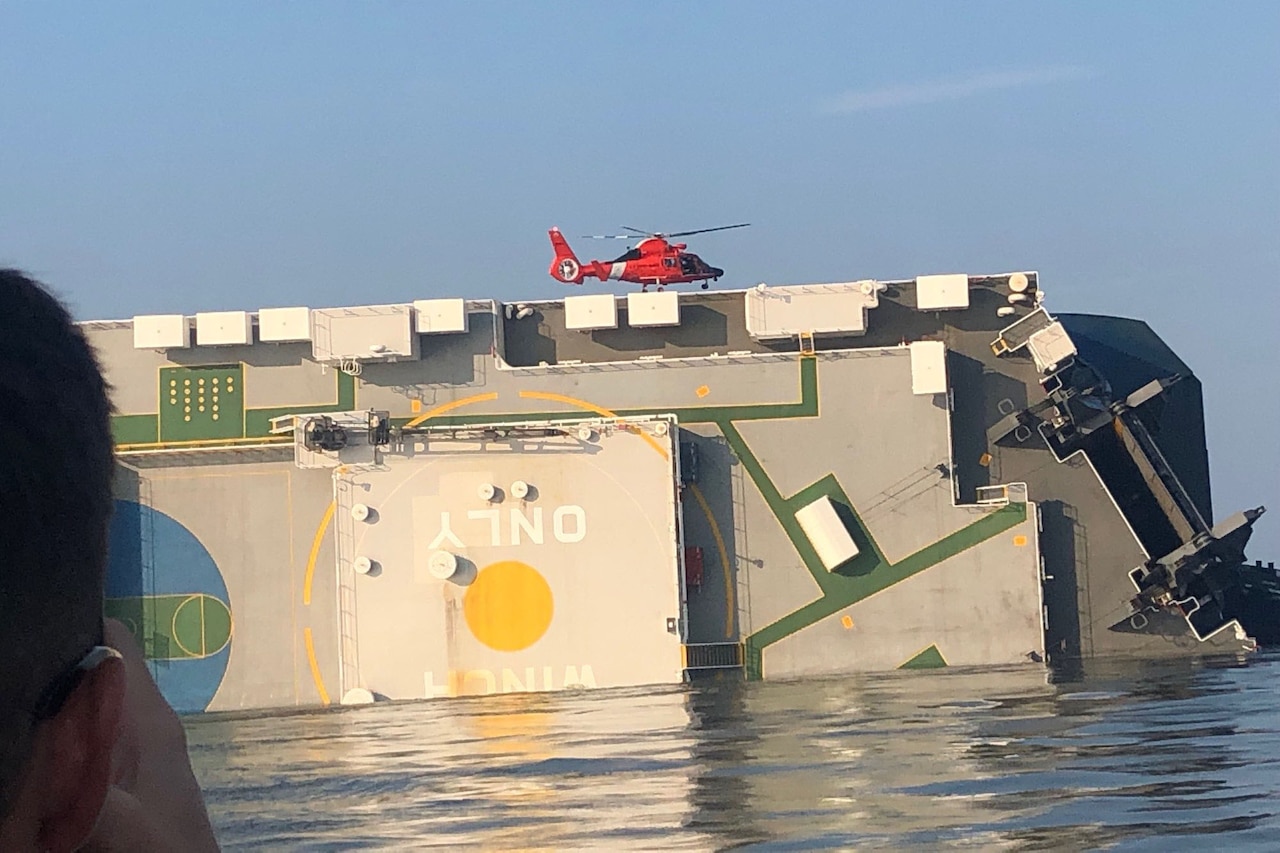 A helicopter flies above a ship on its side.