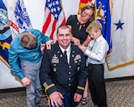 Family replaces rank patches on Army officer's uniform with new rank.