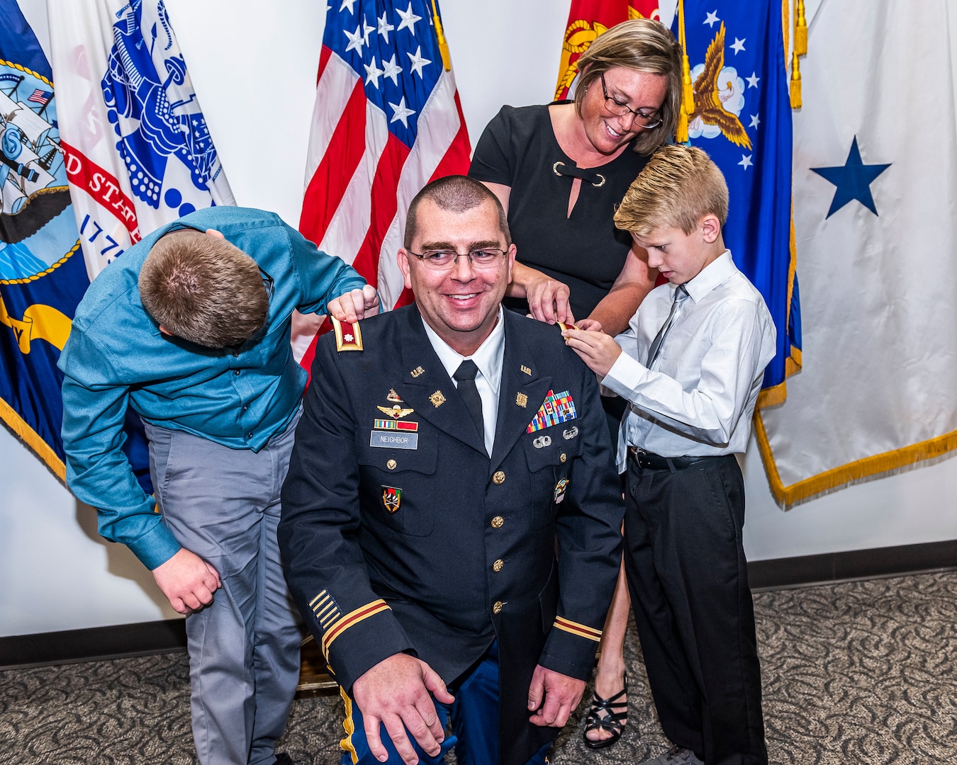 Family replaces rank patches on Army officer's uniform with new rank.