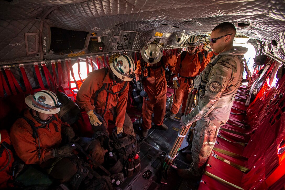 A soldier helps a group of firefighters inside an aircraft.