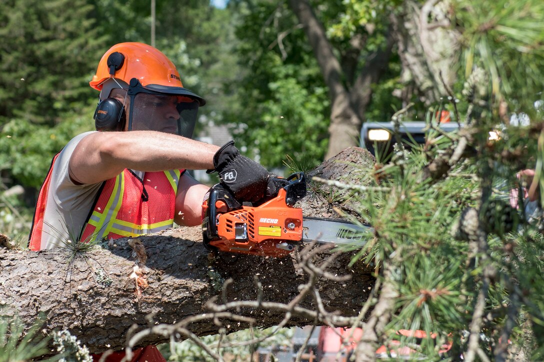 An airman uses a chainsaw on a fallen tree.