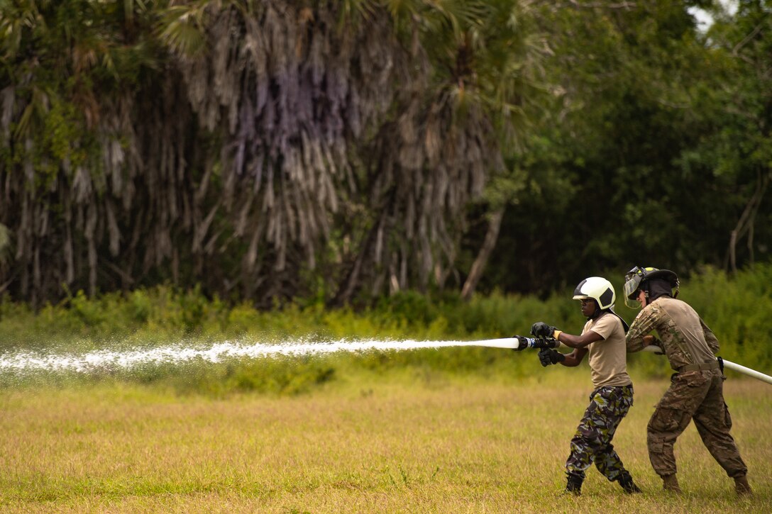 A Kenya Navy firefighter and U.S. Air Force Airman 1st Class Christopher Stillman, 475th Expeditionary Air Base Squadron firefighter, spray a firehose at a cone during a training circuit at Manda Bay, Kenya, Aug. 29, 2019. The training, held by 475th EABS firefighters, was designed to build upon the established partnership between the two nations by enforcing teamwork and endurance while enhancing technical proficiency. (U.S. Air Force photo by Staff Sgt. Devin Boyer)