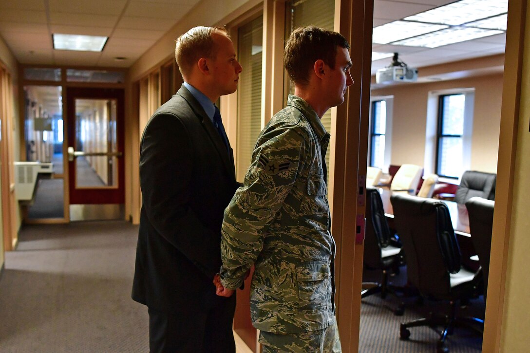 An Airman is walked into an interview room while in handcuffs.