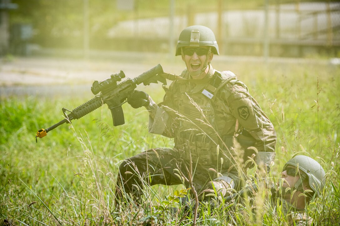 A soldier yells to his squad through yellow smoke as another soldier lies on the ground.