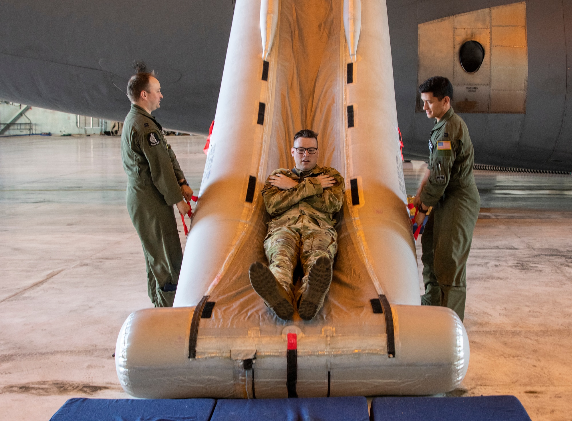 U.S. Air Force Capt. Drew Pagenkopf, left,  tactics flight commander, and Capt. Jose Hinojosa, right, C-5 evaluator aircraft commander, both with the 22nd Airlift Squadron watch as Staff Sgt. Kevin Robinson, 22 AS loadmaster evaluator, uses a C-5M Super Galaxy emergency escape slide Sept. 6, 2019, at Travis Air Force Base, California. Robinson wore a Go Pro camera to record footage of the process to be used to develop a virtual reality training program on aircraft procedures. (U.S. Air Force photo by Heide Couch)