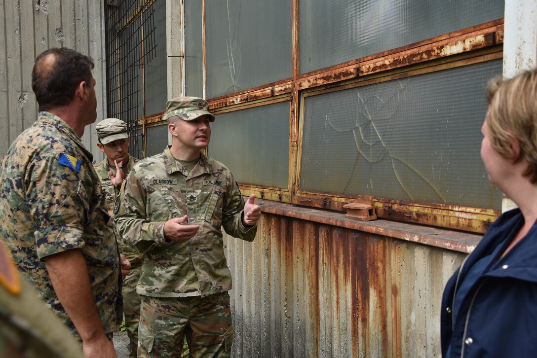 Three service members stand outside a rusty building.