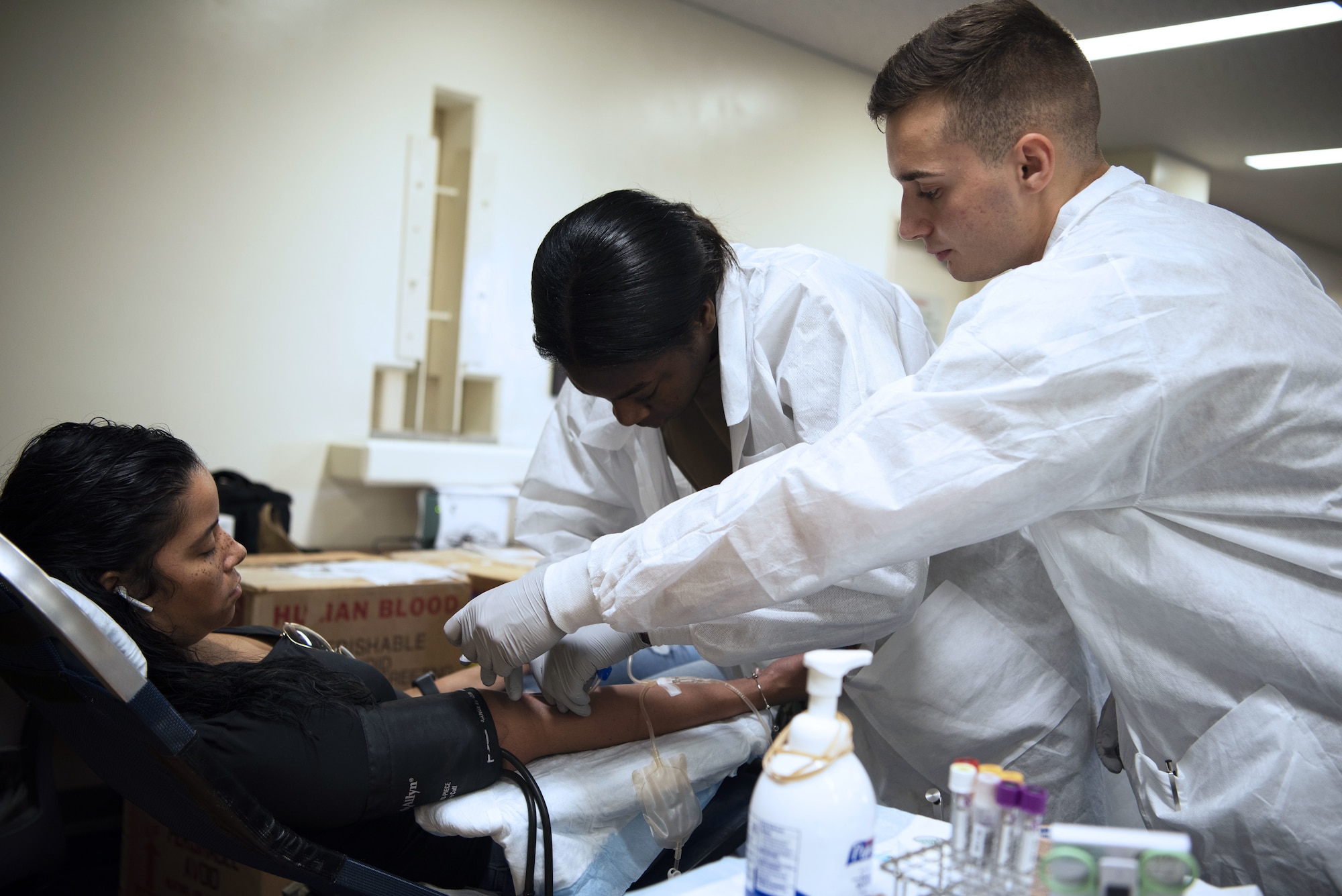 A woman lies down, while a man and woman draws her blood.