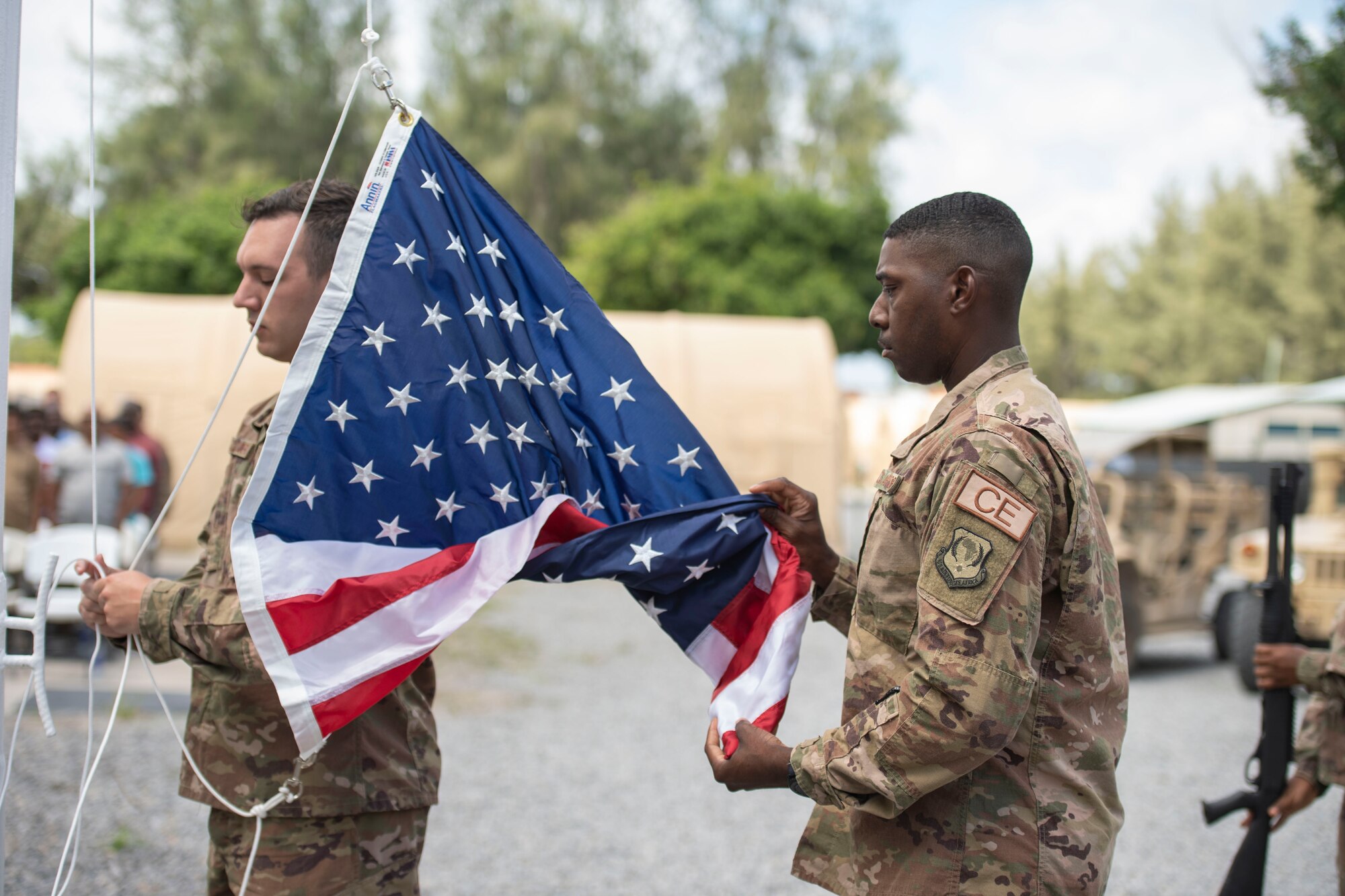U.S. Air Force Staff Sgt. Sidney Dellinger, 475th Expeditionary Air Base Squadron materiel management journeyman, and Staff Sgt. Corey Smith, 475th EABS heating, ventilation, and air conditioning non-commissioned officer in charge, perform flag detail during a ceremony at Camp Simba, Kenya, Aug. 26, 2019. The 475th EABS raised the flag for the first time since the base operating support-integrator mission started in 2017, signifying the change from tactical to enduring operations. (U.S. Air Force photo by Staff Sgt. Lexie West)