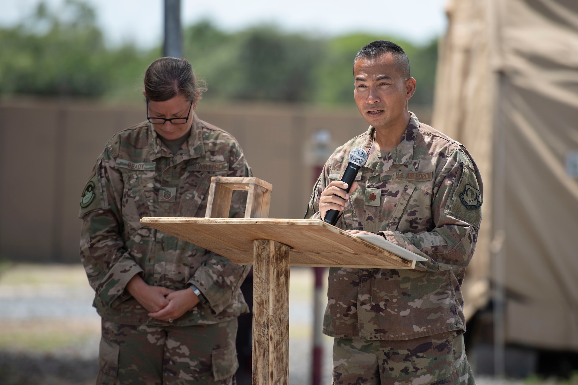 U.S. Air Force Maj. Hoang Nguyen, 435th Air Expeditionary Wing chaplain, gives an invocation while Master Sgt. Shannon Brady, 475th Expeditionary Air Base Squadron first sergeant, bows her head during a flag-raising ceremony at Camp Simba, Kenya, Aug. 26, 2019. The 475th EABS raised the flag for the first time since the base operating support-integrator mission started in 2017, signifying the change from tactical to enduring operations. (U.S. Air Force photo by Staff Sgt. Lexie West)