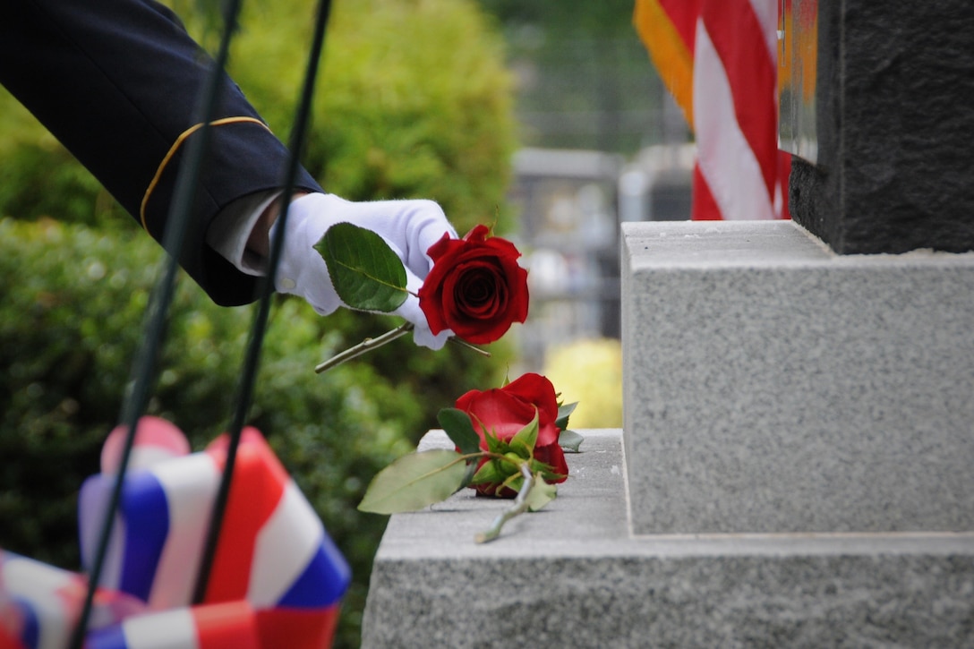 A gloved hand places a rose on a memorial.