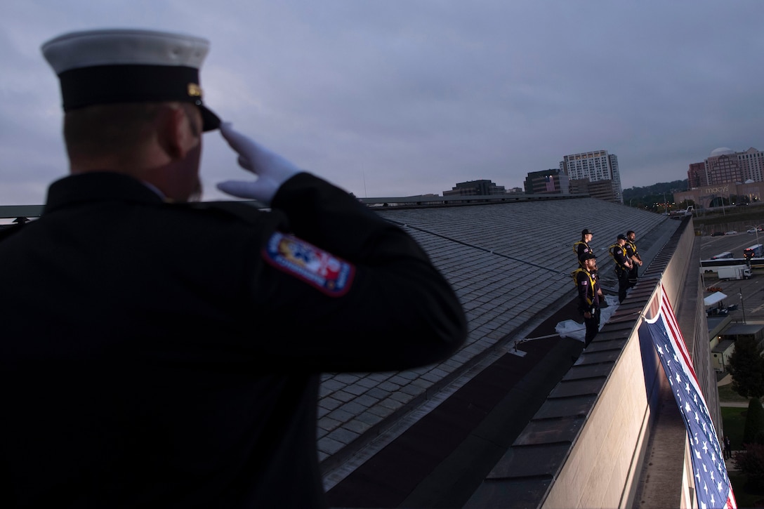 A man salutes on the Pentagon's roof as crew members in the distance stand over an unfurled American flag.