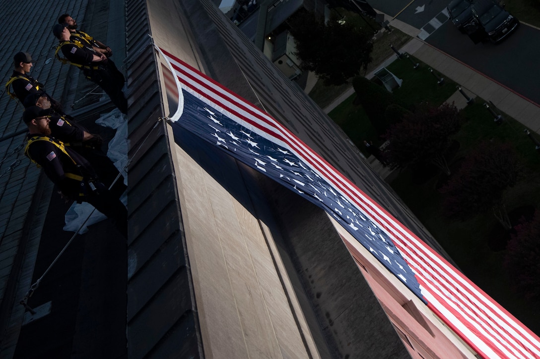Workers in matching uniforms stand on the Pentagon roof overlooking a giant American flag.