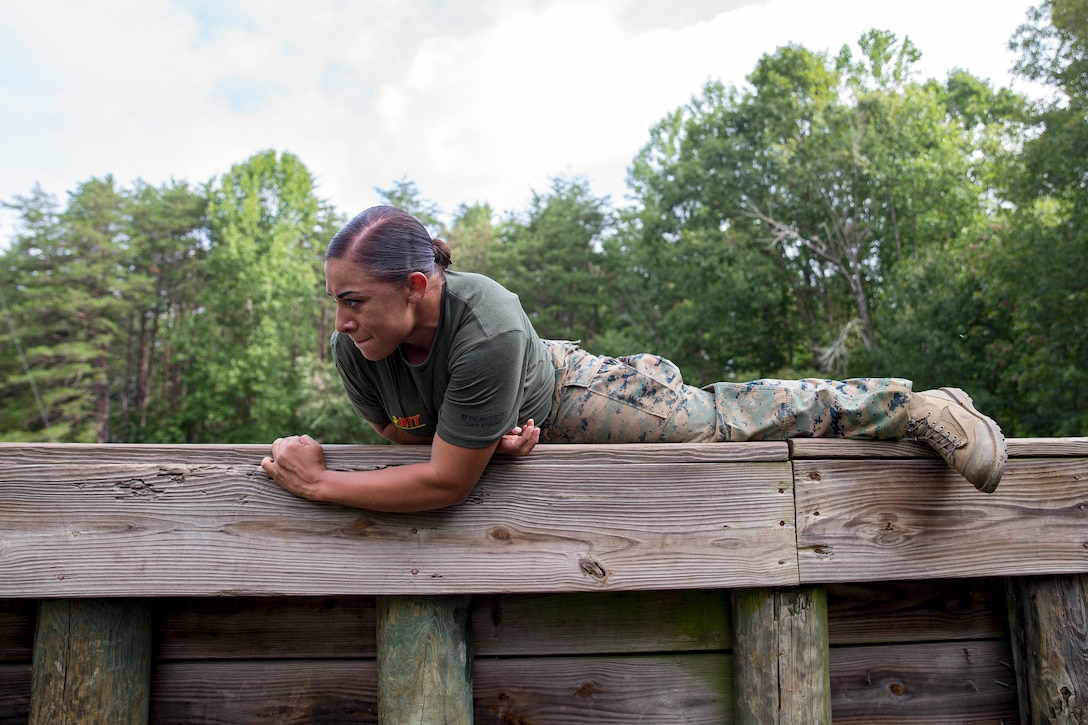 A Marine grimaces while at the top of a wooden obstacle she's scaling.