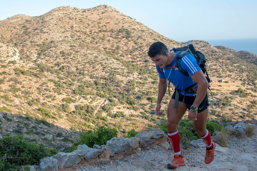 A hiker walks on a trail, with a mountain peak in the distance.