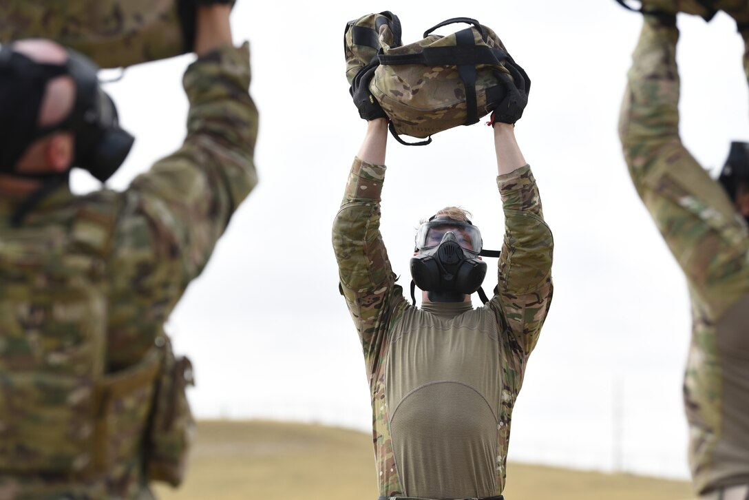 Airmen don their gas masks and complete a set of workouts to include overhead sandbag presses during the Crow Creek Challenge Sept. 6, 2019, at F. E. Warren Air Force Base, Wyo. The heavy bags were also used in other activities like a high-crawl bag toss and numerous calisthenic workouts. This obstacle was just one of many physical obstacles security forces members took part in during the challenge. (U.S. Air Force photo by Senior Airman Nicole Reed)