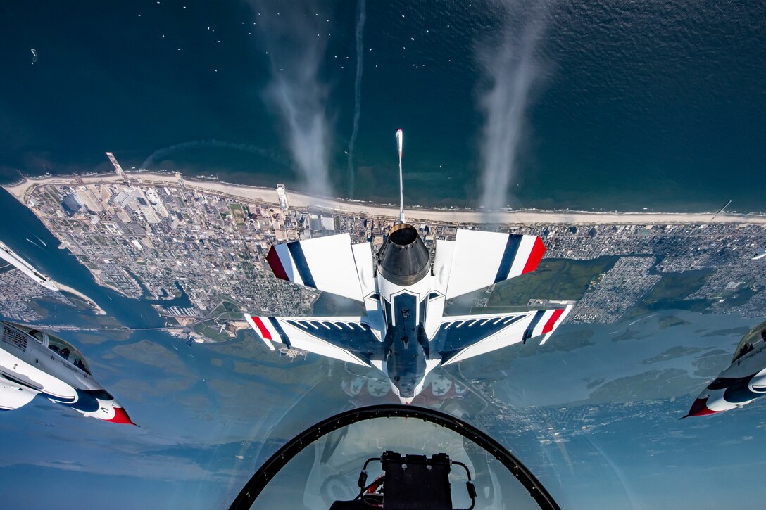 A view from the cockpit of a military jet looks out at other jets and the ocean coastline.