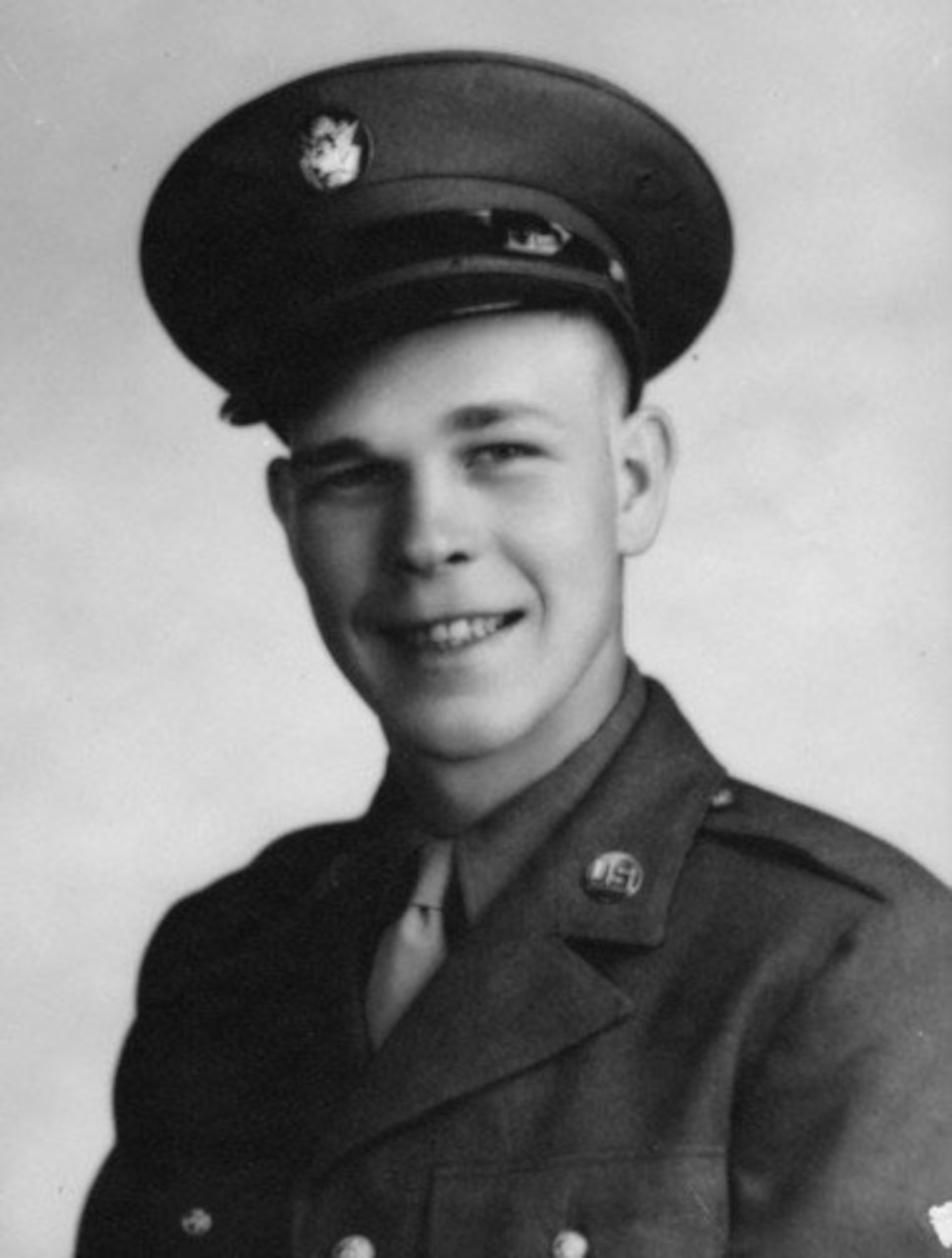 A young man smiles in his Army dress uniform jacket and cap.