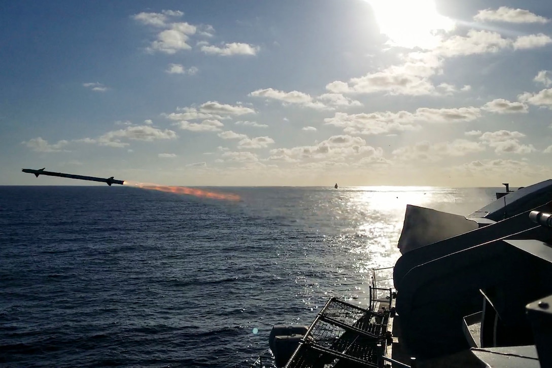 A missile flies through the air over the ocean after being launched from a military ship.