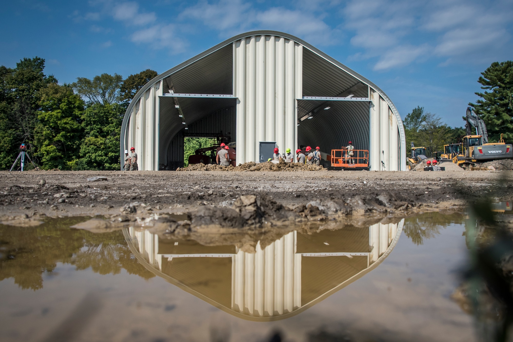 Wide landscape photo of a building and military members with its reflection in a puddle of water.