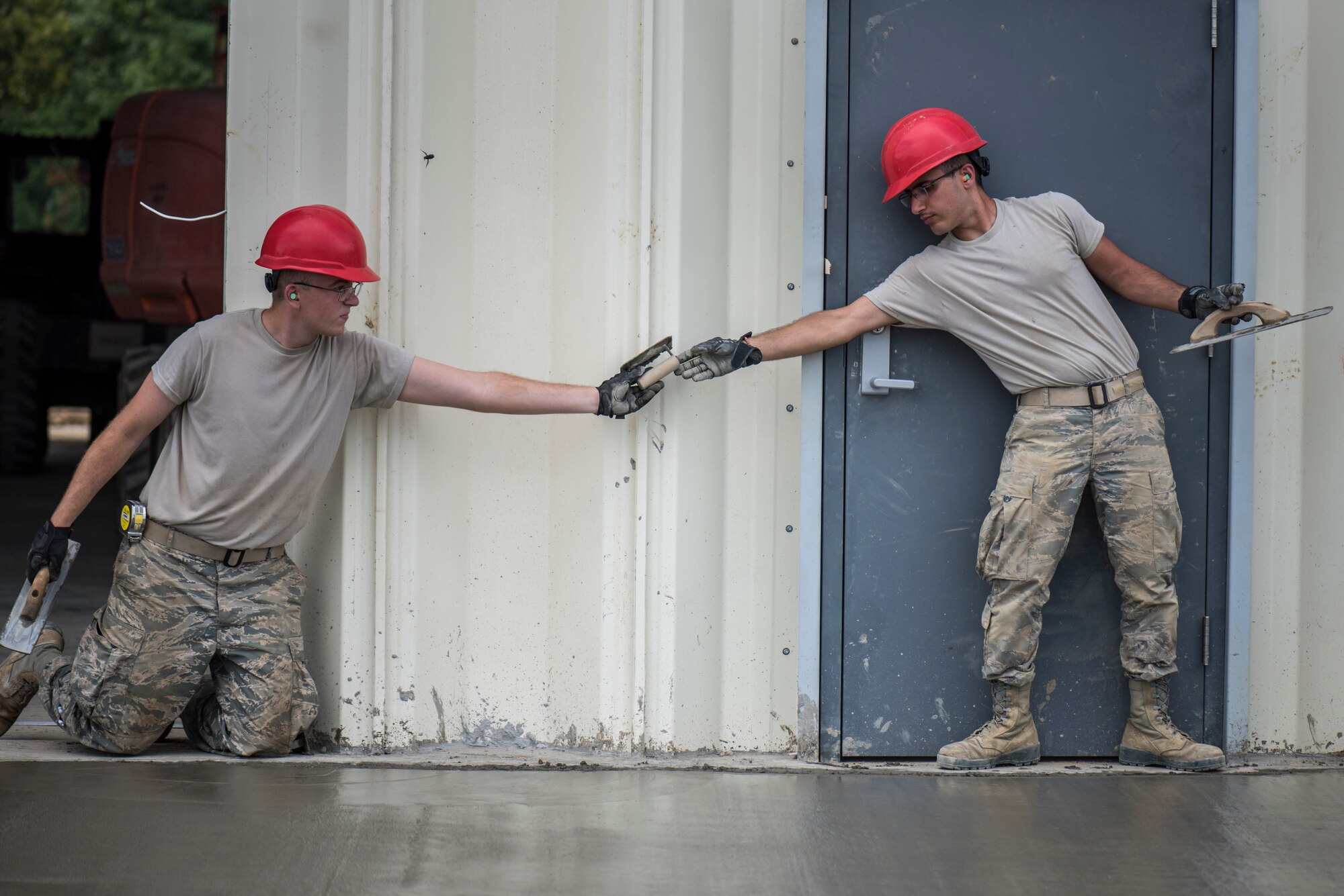 Photo of two military members passing equipment over wet cement