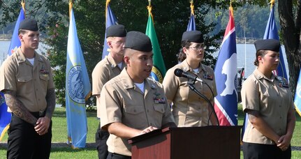 IMAGE: DAHLGREN. Va. (Sept. 11, 2019) – Navy chief select David Hernandez shares a story of heroism in response to the terrorist attacks and ensuing tragedies on 9/11. Hernandez was one of seven chief select ‘heroism readers’ based at commands located on Naval Surface Facility Dahlgren who recounted acts of heroism on that tragic day in our nation’s history.

Hernandez – reading to military, first responders, government and contractor personnel gathered to honor the victims of 9/11 – recounted that:
“Fifteen minutes after takeoff from Boston, American Airlines Flight 11 was hijacked by five al Qaeda terrorists and sharply changed its flight path away from Los Angeles to New York City. Using crew telephones, flight attendants Betty Ong and Amy Sweeney calmly relayed information to their colleagues on what was unfolding that morning. Those on the other end of the line were astonished at their calm demeanor and professionalism at the time. At least 20 minutes before the plane crashed into the North Tower, American Airlines had the names, addresses, and other information on three of the five hijackers, details that would help the FBI get a jumpstart on the investigation.”