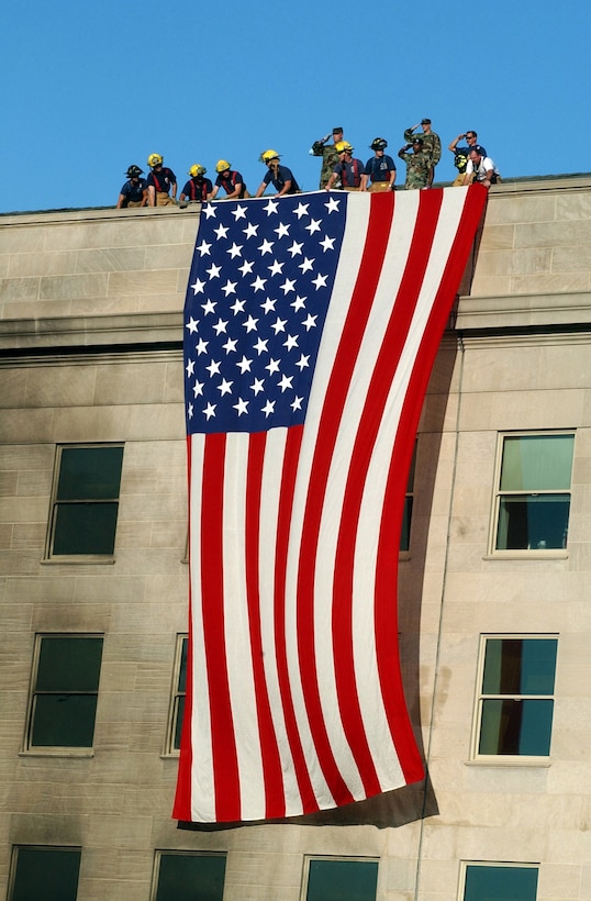Military members, firefighters and rescue workers unfurl a huge American flag over part of the Pentagon, covering windows on two floors.