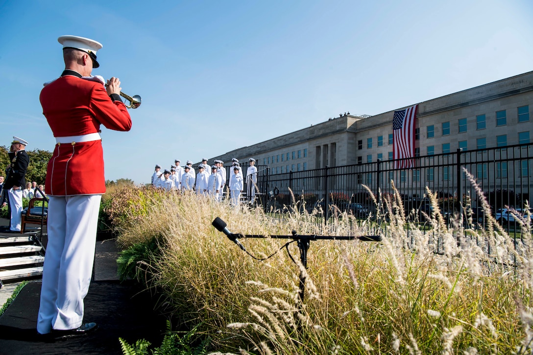A Marine Corps bugler stands and performs facing the Pentagon, as other troops stand in formation nearby.