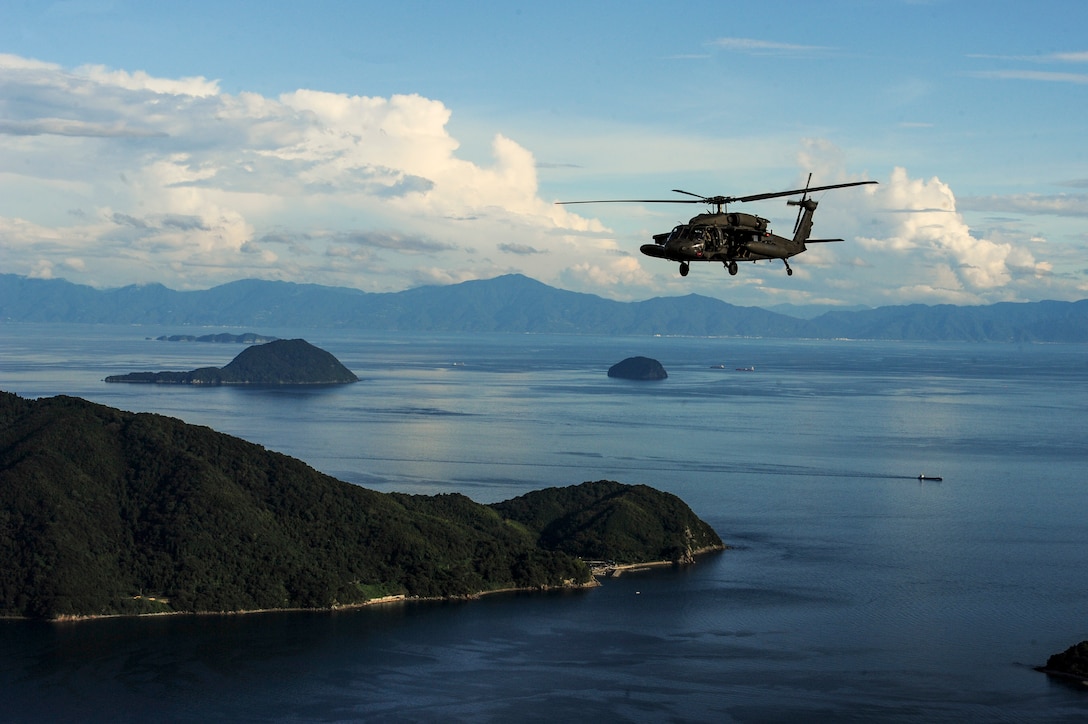 A helicopter flies over blue waters studded with wooded islands.