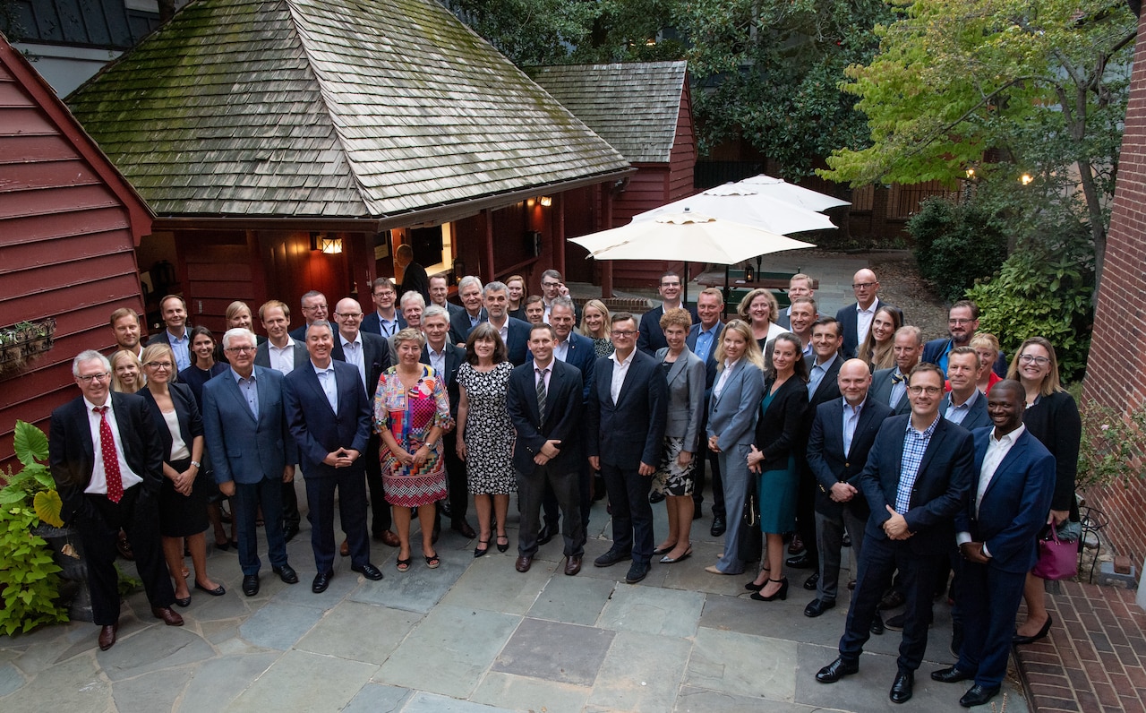 Several dozen individuals stand in a semicircle formation in a courtyard