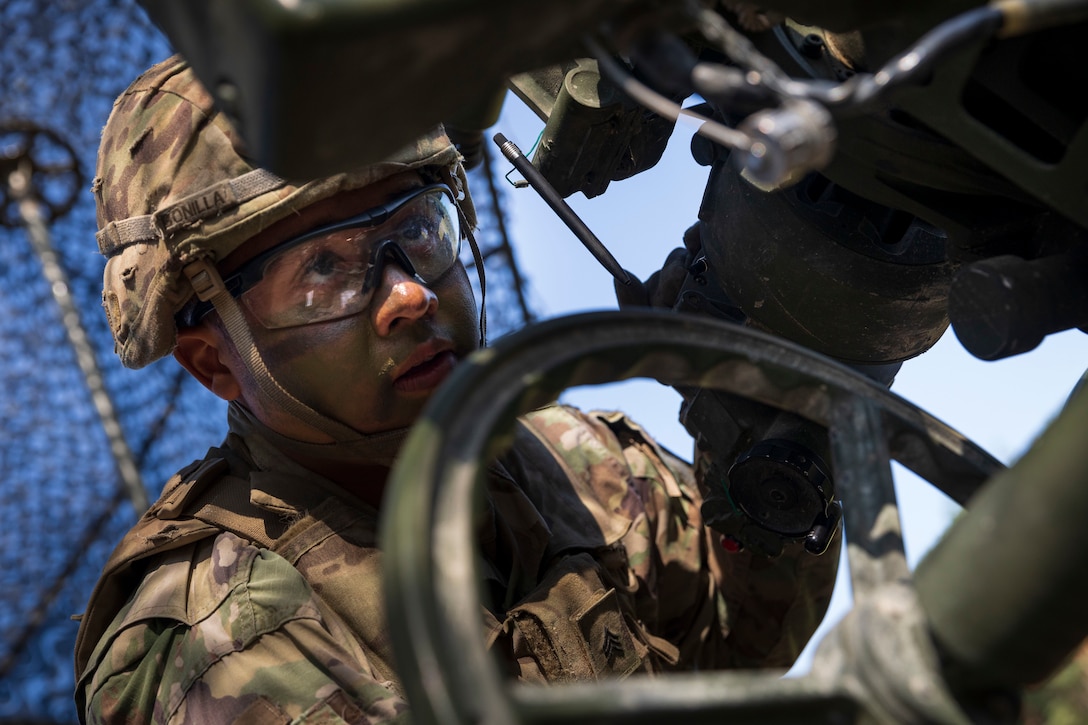 A soldier focuses his eyes on part of a large military weapon.