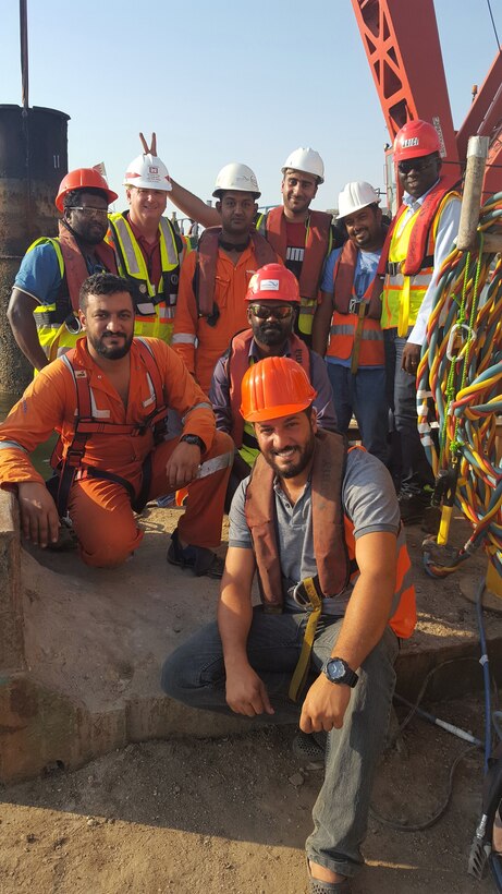 Photo of 8 construction workers in a group shot. One is being given the rabbit ears gesture used in photos.